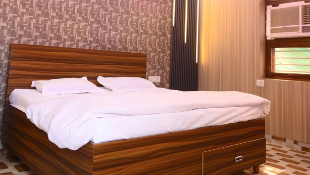 A neatly made bed in a room with a patterned wall, a ceiling fan, and a window with blinds. - Apartment #2 at Sadhnaaa Apartments Agra (Agra)