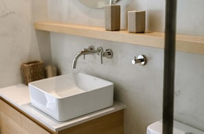 Un baño con un lavamanos blanco, un tocador de madera y una pared de mármol.