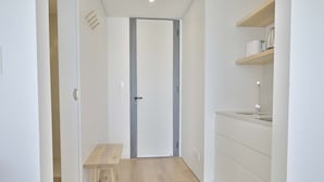 A narrow hallway with a wooden bench, a white door, and a kitchen area with a sink and shelves. - Punta Cantera Suites de Mar (Mar del Plata)