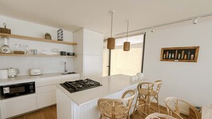 A modern kitchen with white cabinetry, a central island, wicker chairs, and a dining table. - Punta Cantera Suites de Mar (Mar del Plata)