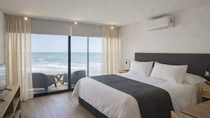 A hotel room with a large bed, a desk, a chair, and a view of the ocean. - Punta Cantera Suites de Mar (Mar del Plata)