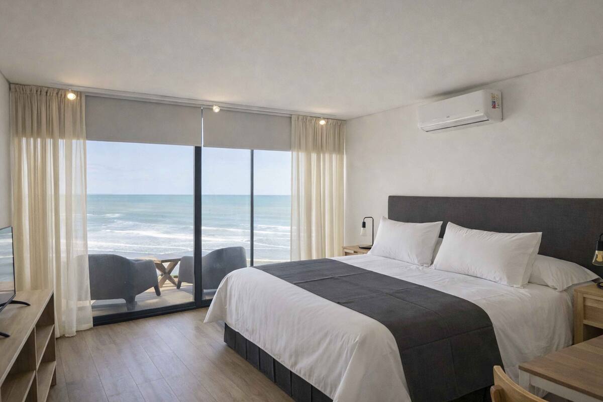 A hotel room with a large bed, a desk, a chair, and a view of the ocean.