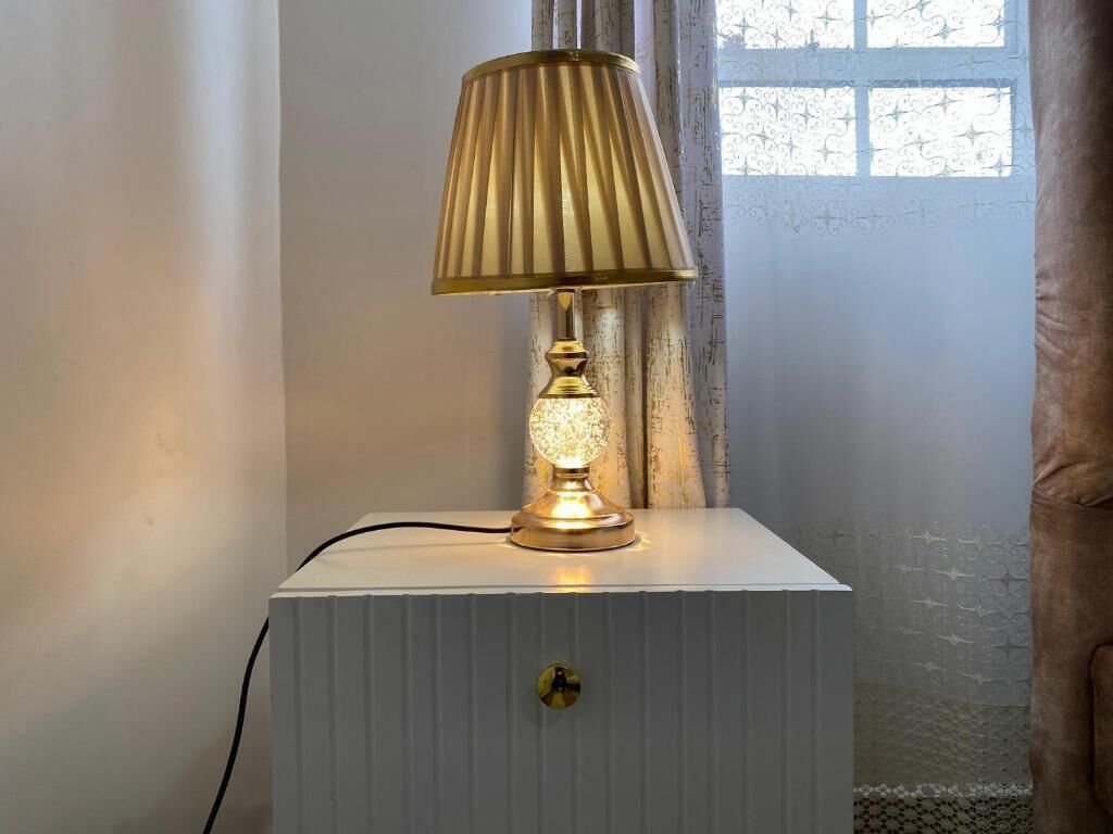 A bedside table with a lamp, a keyhole, and a window with curtains.