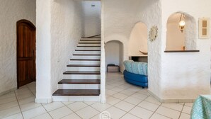 A staircase leading to a second floor, white walls, a wooden door, a blue sofa, and a hanging light fixture.