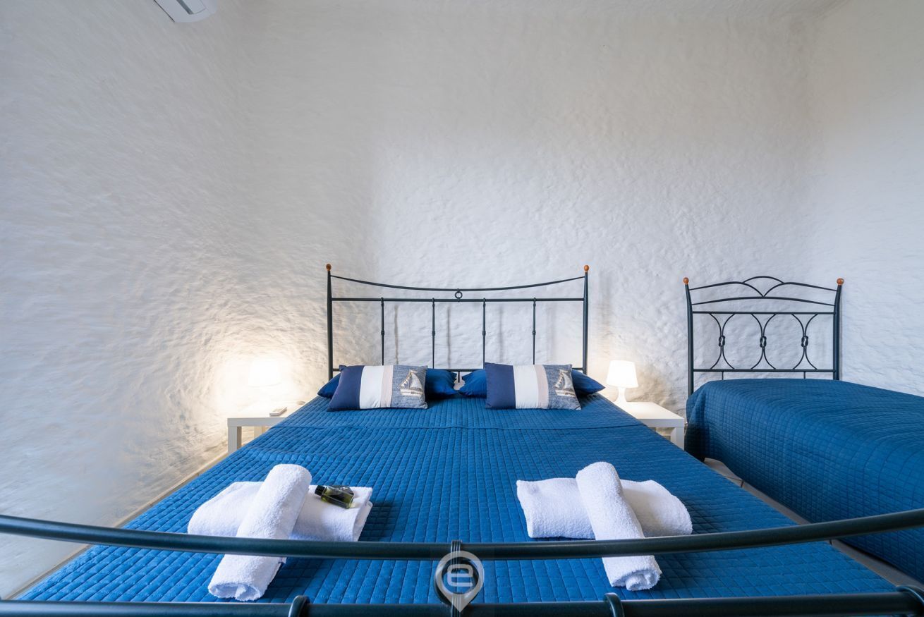 Quarto com cama, duas almofadas, mesa de cabeceira e abajur.