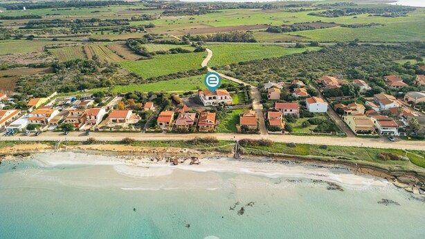 An aerial view of a coastal village with houses, a beach, and agricultural fields.