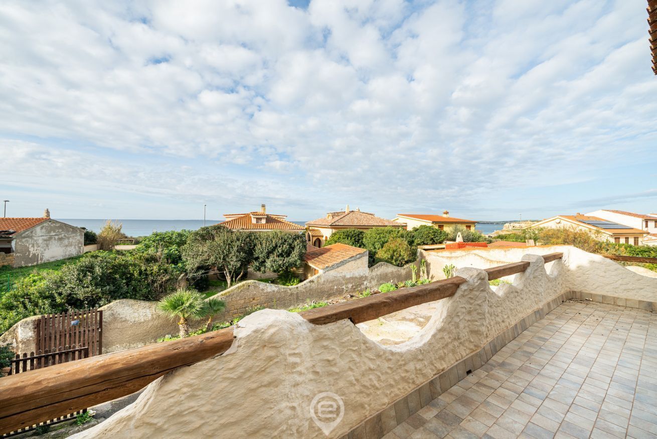 A coastal property with a terrace overlooking the sea, featuring traditional architecture and a stone wall.