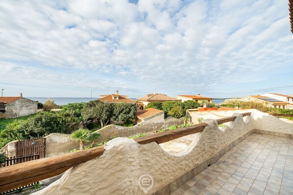 A coastal property with a terrace overlooking the sea, featuring traditional architecture and a stone wall.