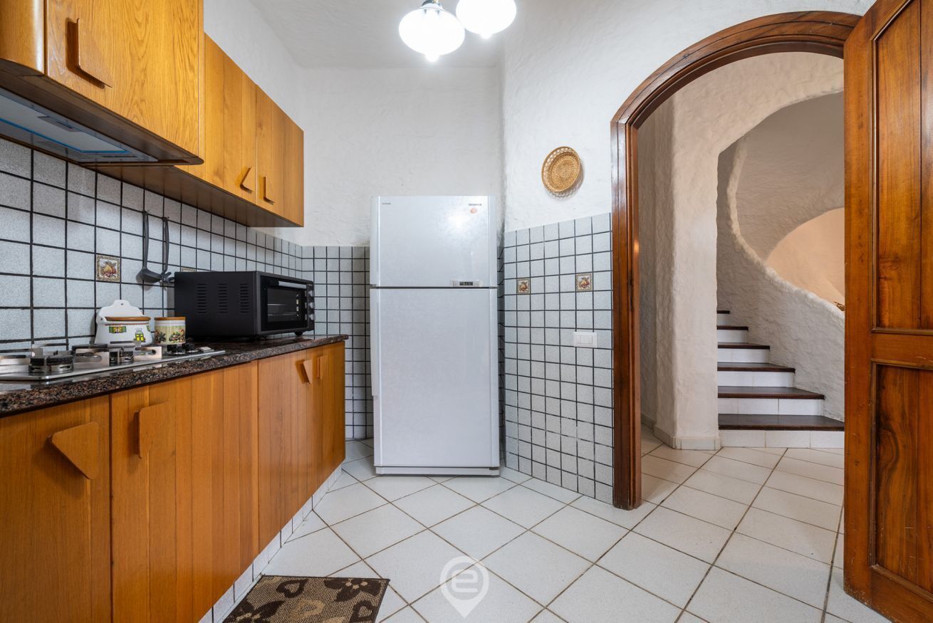 A kitchen with wooden cabinets, a black microwave, a white refrigerator, and a tiled backsplash.