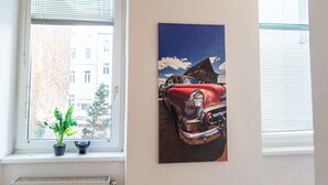 A window with blinds, a potted plant, and a painting of a vintage car. - Modern Long-Stay 3-Room Apt near Wiener Stadthalle (Vienna)