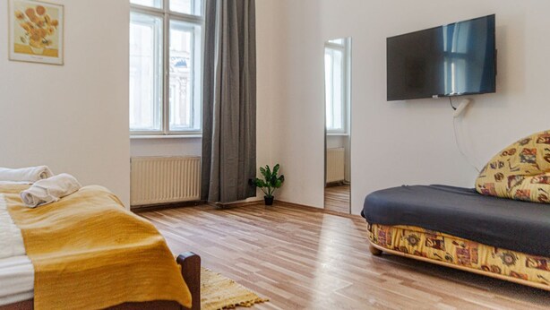 A room with a bed, a sofa, a TV, a window with curtains, and a plant. - Modern Long-Stay 3-Room Apt near Wiener Stadthalle (Vienna)
