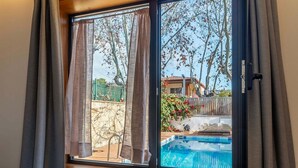 A window with curtains, a view of a swimming pool, and a house in the background.