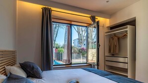 A bedroom with a bed, a window with curtains, a wardrobe, and a view of the outside.