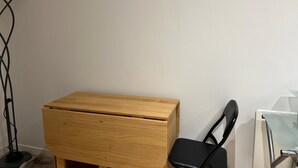 Ein kleiner, hölzerner Schrank mit Schublade, ein schwarzer Stuhl und eine Stehlampe in einer Ecke des Raumes.