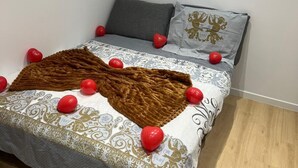 Ein ordentlich bezogenes Bett mit einer gemusterten Tagesdecke, einer braunen Sofadecke und roten Dekokugeln.