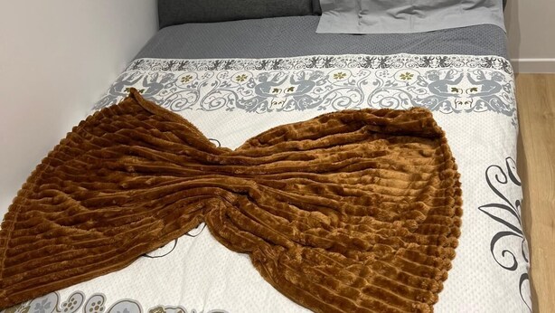 Ein Bett mit einem gemusterten Überwurf, einer braunen, strukturierten Decke und einem Kissen mit einer Goldverzierung.