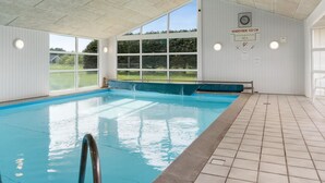 Una piscina interior con ventanas transparentes, un indicador de profundidad visible y suelo de baldosas.