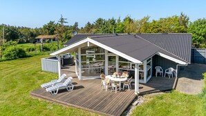 Una casa moderna con un porche cubierto, un jacuzzi y una terraza con sillones de descanso.