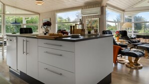 Cocina moderna con una isla grande, techo de madera y amplios ventanales con vistas a la vegetación.
