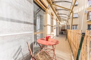 A corridor with a red metal table and chairs, large windows, and a bamboo fence. - Asinari Retreat [San Marzano] (Roma)