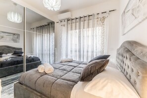 A modern bedroom with a large bed, a dark sofa, and a mirrored wardrobe. - Asinari Retreat [San Marzano] (Roma)