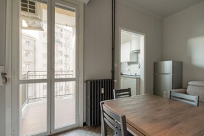 A room with a wooden table, a chair, a radiator, a refrigerator, and a door leading to a balcony. - GuestHost - A comfortable and welcoming 45 square meters apartment, perfect for four people, located on the fourth floor of a building without an elevator.The property is located in the Navigli district, one of Milan's liveliest areas: guests can enjoy r (Milan)