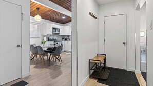 Et moderne køkken med hvide skabe, et træloft og et spiseområde med et bord og stole.