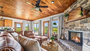 A spacious living room with a stone fireplace, leather sofas, and a ceiling fan. - New 2025–5 Mi Dollywood–Mtn Views–1-Step–Pets (Sevierville)