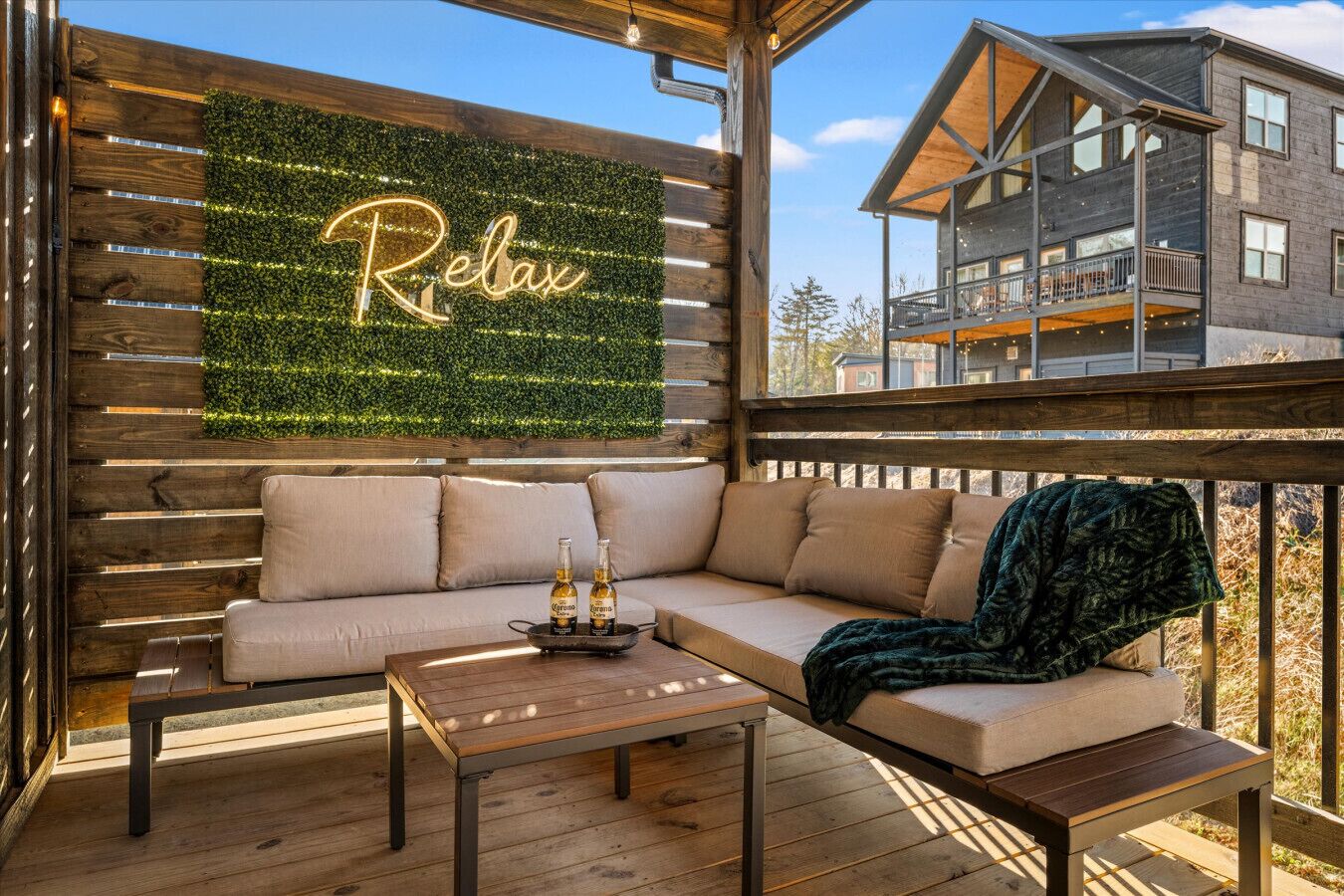 A wooden deck with a sofa, a table with bottles, and a neon sign that reads "Relax".