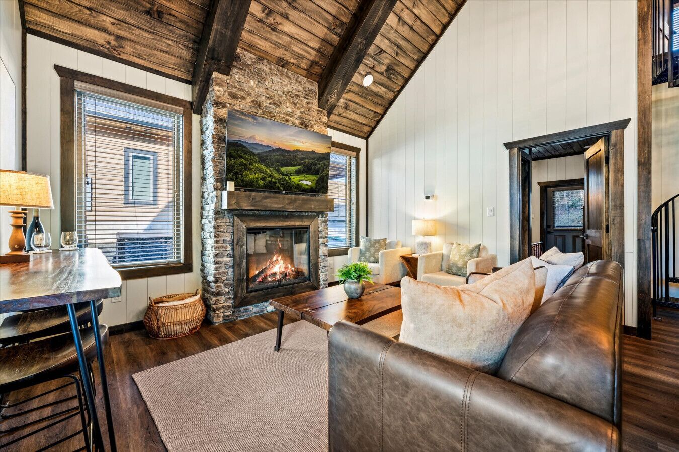 A cozy living room with a stone fireplace, leather sofa, and a large TV.