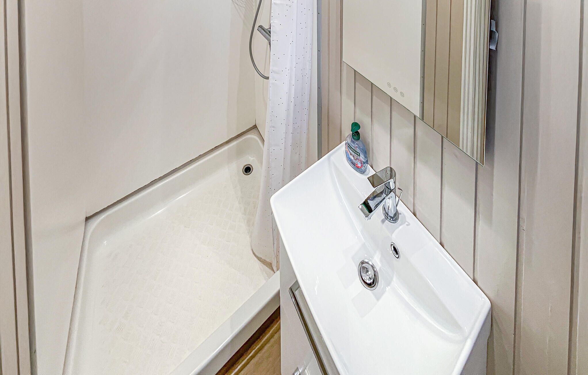 A bathroom with a white sink, a mirror, and a shower area.