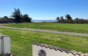 A grassy field with a gravel path, a white building with a tiled roof, and a view of the ocean.
