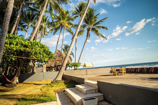 A beach with palm trees, a thatched-roof structure, and a row of wooden chairs along the shore.