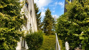Un escalier menant à un bâtiment à l’extérieur blanc, entouré de verdure et sous un ciel dégagé.