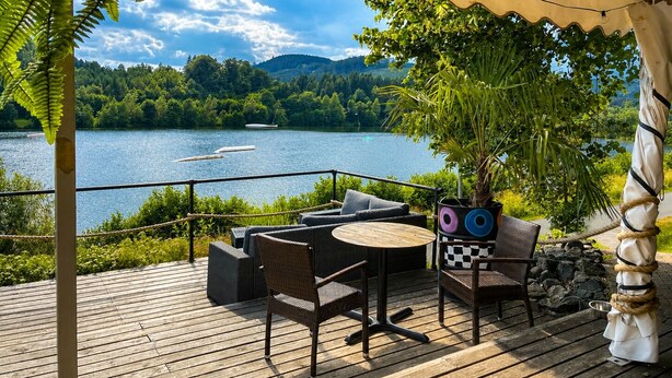 Une terrasse dotée de mobilier d’extérieur, offrant une vue sur un lac et entourée de verdure et de montagnes.