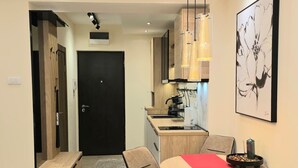 A modern dining area with a round table, two chairs, a red table runner, and a kitchen in the background. - Elegant Apartment in Belgrade City Center – Stari Grad (Beograd)