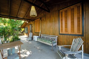 A wooden porch with a bench, chairs, and a fan.