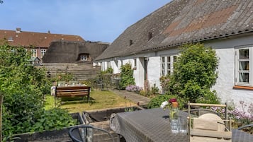 Et hyggeligt udendørs opholdsområde med en træbænk, metalstole og et bord dækket med dug.