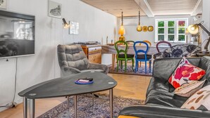 Una sala de estar moderna con un televisor, un área de comedor con sillas coloridas y un sofá con cojines estampados.