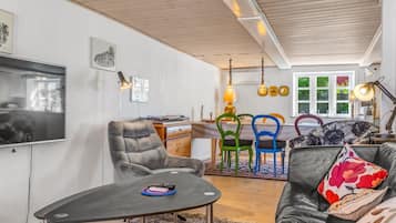 Una sala de estar moderna con un televisor, un área de comedor con sillas coloridas y un sofá con cojines estampados.