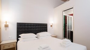 Hotellihuone, jossa on suuri sänky, kaksi yöpöytää, vaatekaappi ja suihkutila.