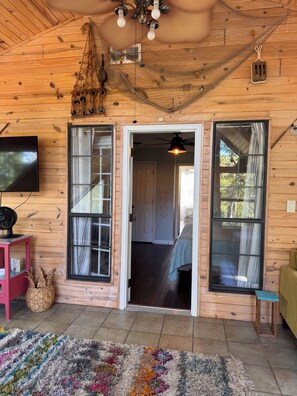 A wooden interior with a television, a ceiling fan, and a door leading to another room.