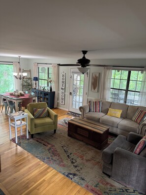 A living room with a sofa, armchairs, a coffee table, a dining table, and a chandelier.