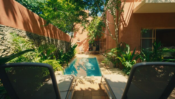 Zona de piscina con dos sillas de descanso frente a ella, rodeada de abundante vegetación y un muro de piedra.