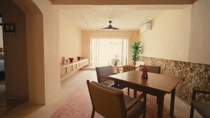 Un comedor con una mesa de madera, sillas de mimbre, un ventilador de techo y una pared decorativa de piedra.