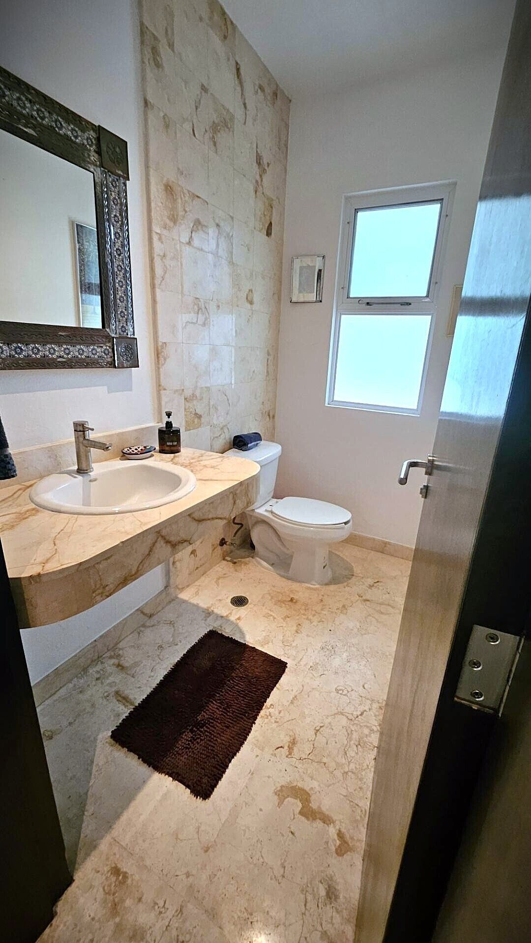 Baño con dos lavamanos, inodoro, espejo grande y ventana.