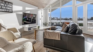 Een moderne woonkamer met een grote televisie, comfortabele zitplaatsen en uitzicht op een besneeerd landschap door grote ramen.