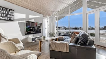 Un salon moderne doté d’un grand téléviseur, de sièges confortables et offrant une vue sur un paysage enneigé grâce à de grandes fenêtres.