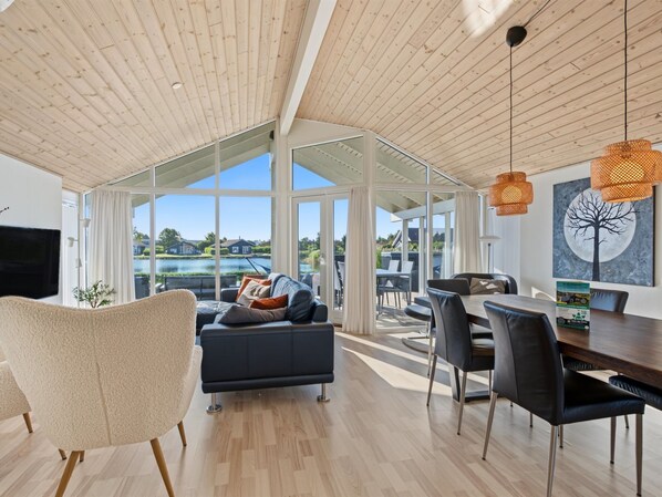 A spacious living area with a large window, a sofa, a dining table, and a television.