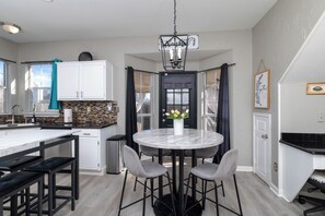 A modern kitchen with a marble island, black bar stools, and a central dining table with chairs. - Fire Pit, Kids Toys + Fenced Yard - Family Getaway (Grand Prairie)